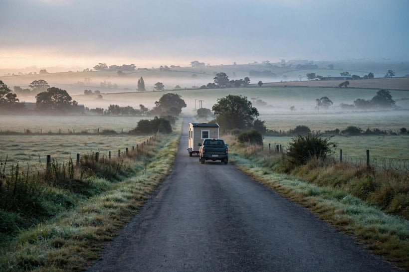 how to keep your tiny house safe: an unanchored tiny house being towed away down a rural road at dawn