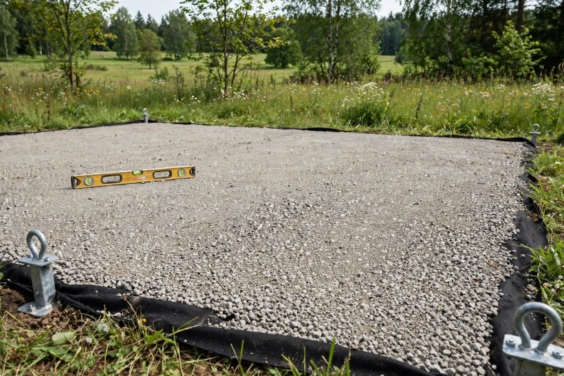 how to prepare land for a tiny house: compacted gravel pad on geotextile fabric with tie-down anchors