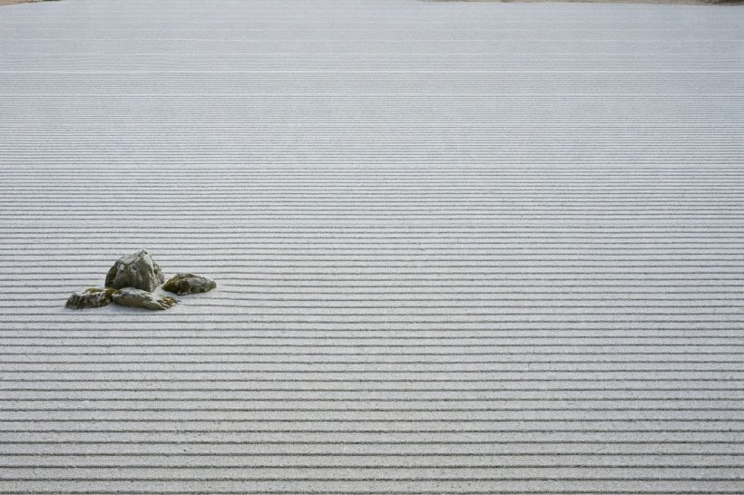 Japanese zen rock garden: a wide empty field of raked gravel with one small off-centre rock group