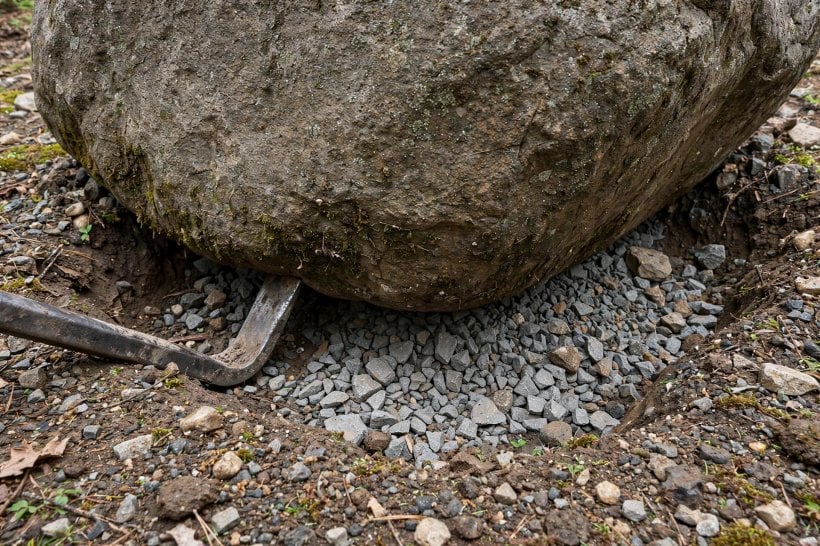 Laying Out Big Landscape Rocks: a pry bar nudging a boulder on its crushed-stone bed