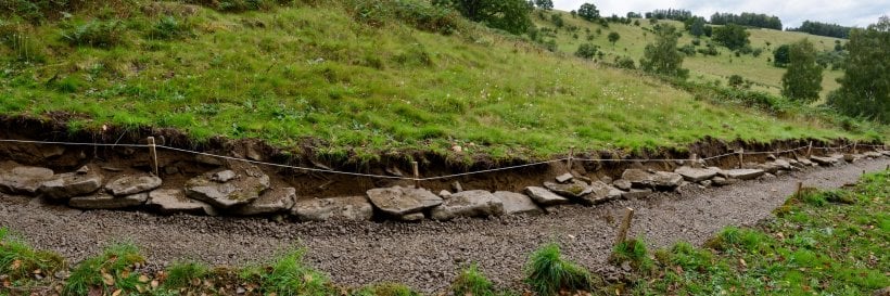 natural rock retaining wall: an excavated trench with compacted gravel base and the largest foundation stones set half-buried