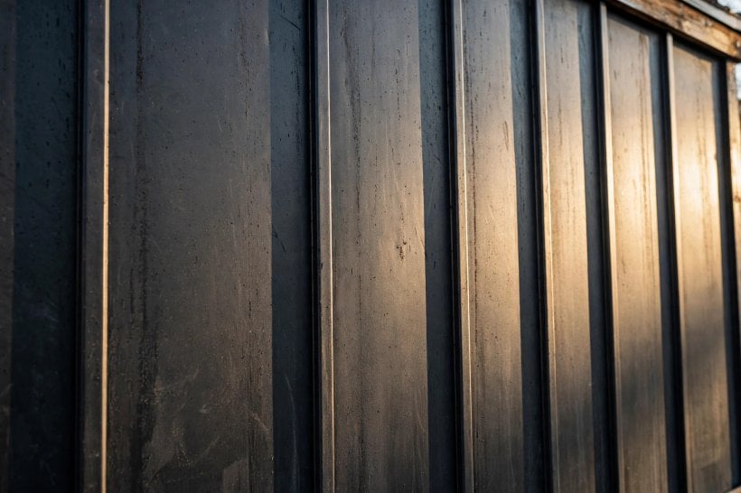 siding weight and durability comparator: dark standing seam metal siding panels on a tiny house wall