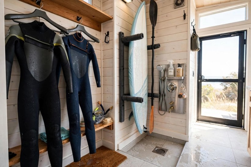 tiny house floor plans with mudrooms: wetsuits on wide hangers and boards on padded arms beside a freshwater rinse station