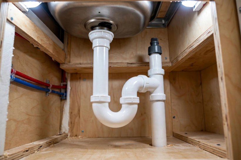 tiny house plumbing: a white PVC drain pipe and P-trap fitted under a tiny house sink
